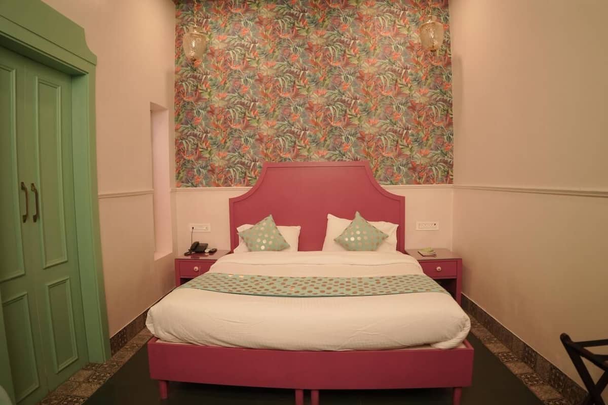 A bedroom with a bed, nightstands, a green wardrobe, and a floral wallpaper.