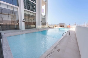An indoor swimming pool with clear blue water, surrounded by a glass wall and a white tiled deck. - JVC 1 bed Sleeps 2 With Private Balcony (Dubai)