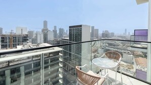 A high-rise building with a glass balcony, wicker chairs, and a clear view of the cityscape. - JVC 1 bed Sleeps 2 With Private Balcony (Dubai)