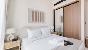 A neatly made bed with white linens, a bedside table with a lamp, and a large mirror. - JVC 1 bed Sleeps 2 With Private Balcony (Dubai)