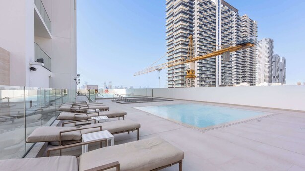 A rooftop pool area with lounge chairs and a view of high-rise buildings under construction. - JVC 1 bed Sleeps 2 With Private Balcony (Dubai)