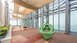 Un intérieur moderne avec un plafond haut, de grandes fenêtres et une sculpture géométrique verte.