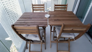 Une table à manger en bois, avec quatre chaises, un plateau blanc et une vue sur de hauts immeubles à travers une porte vitrée.