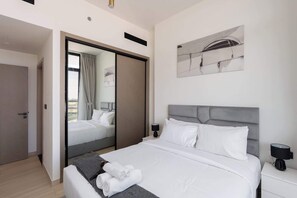A modern hotel room with a large bed, a grey headboard, and a painting on the wall. - JVC Apartment Sleeps 4 in a Great Location (Dubai)