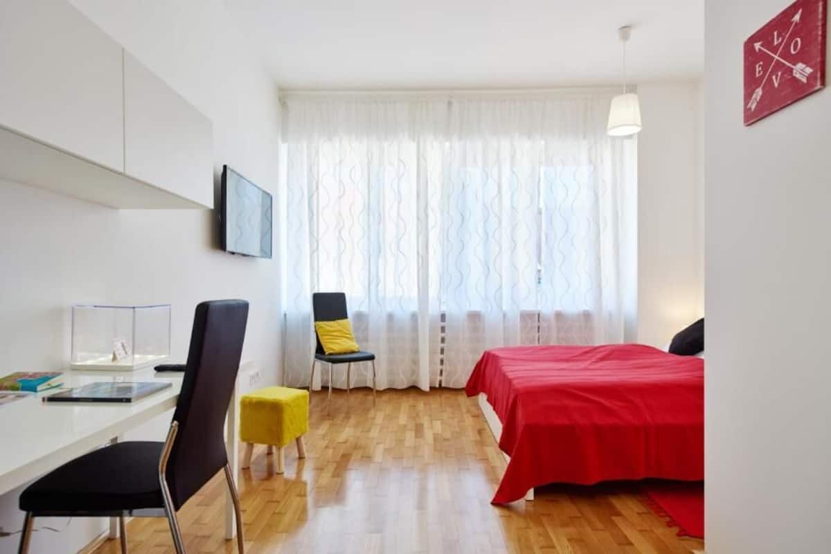 Una stanza con un letto, una scrivania, una sedia e una finestra con tende.