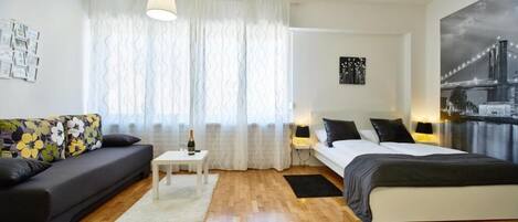 Un dormitorio moderno con cama, sofá, una mesita y una ventana con cortinas.