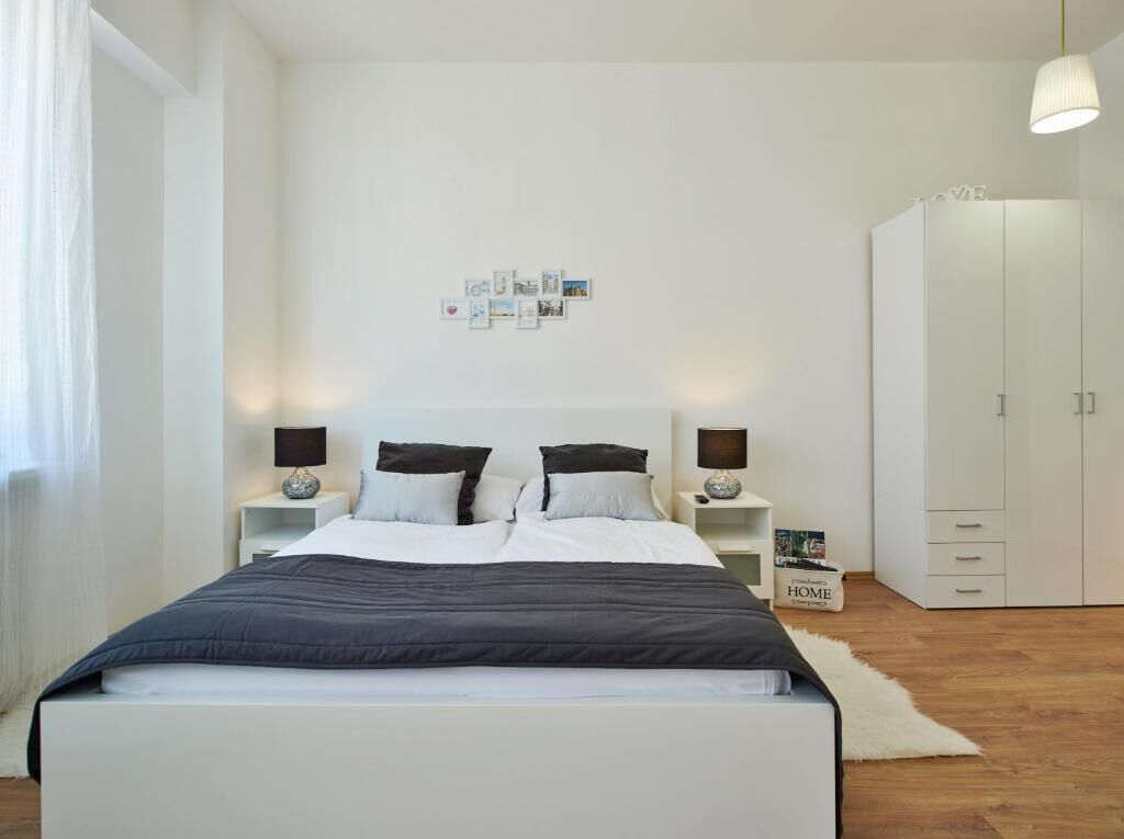 A modern bedroom with a large bed, two bedside tables with lamps, a wardrobe, and a wall with framed pictures.