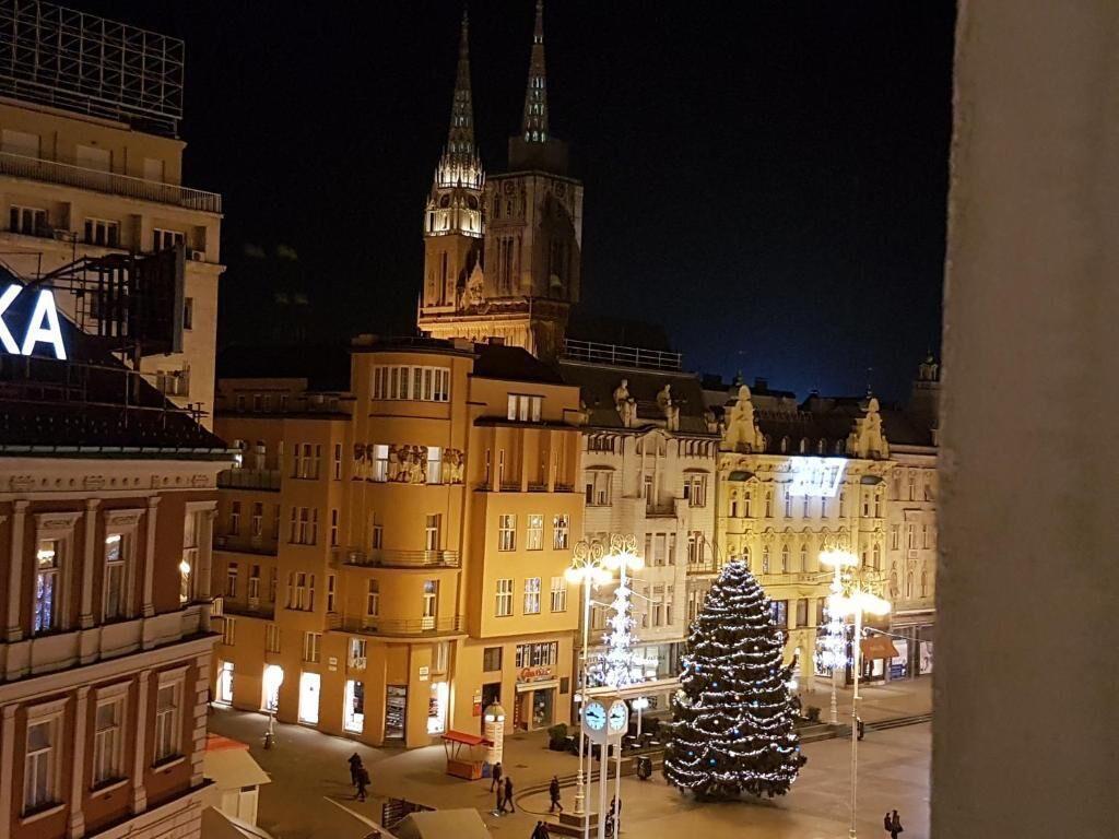 Et natteligt udsigt over et bytorv med et stort juletræ og en fremtrædende domkirke i baggrunden.