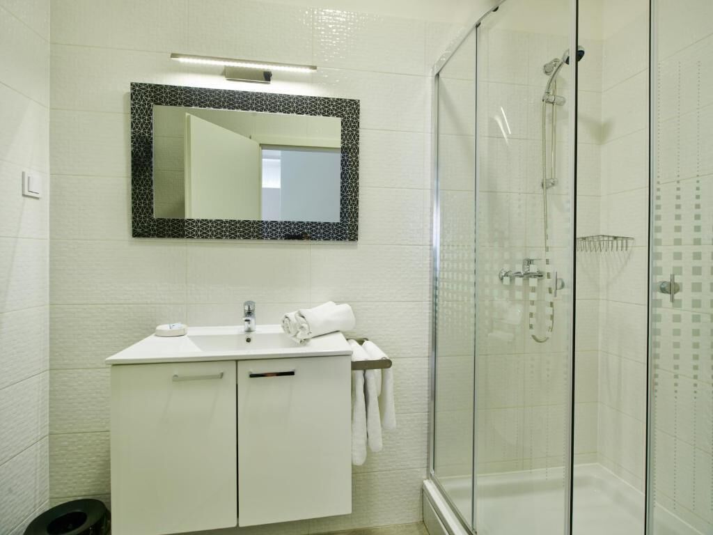 Un bagno moderno con doccia vetrata, un lavandino bianco con specchio sopra e un portasciugamani.