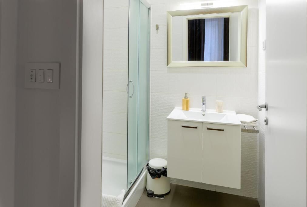 A bathroom with a glass shower enclosure, white sink, and a mirror above it.