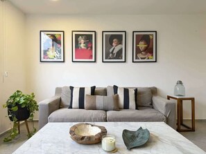 A living room with a beige sofa, a coffee table with decorative items, and three framed artworks on the wall.