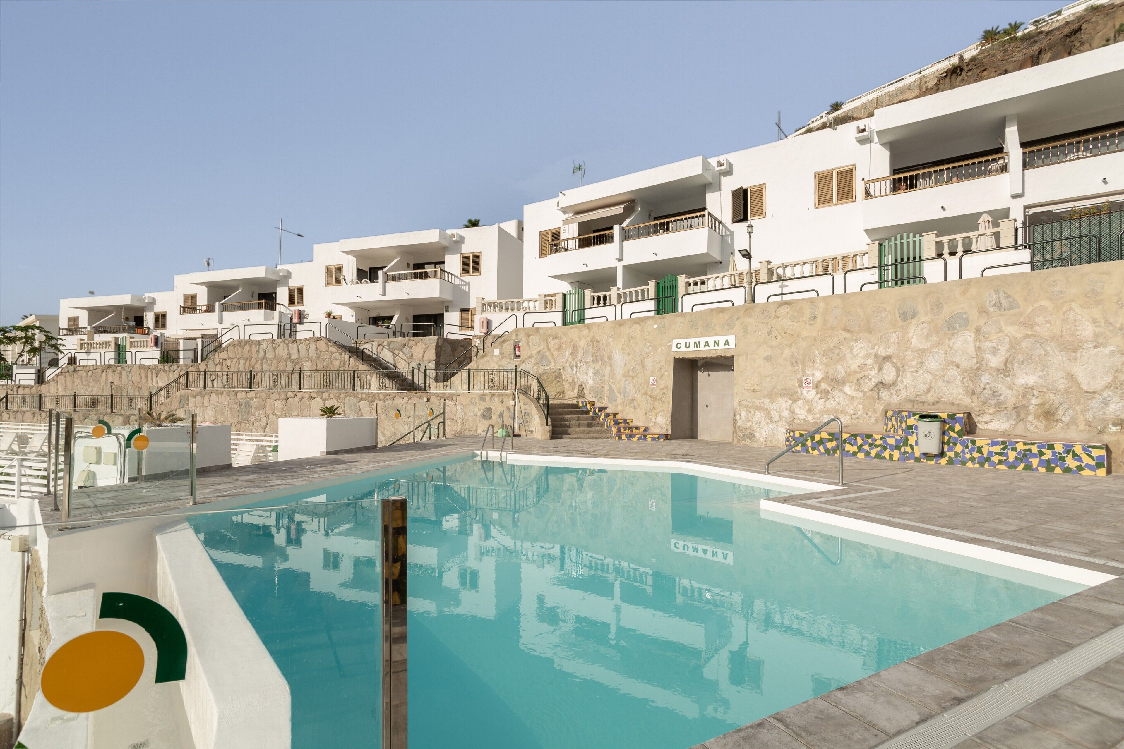 Une piscine avec un mur en pierre et, en arrière-plan, un bâtiment portant l’inscription « CUMANA ».