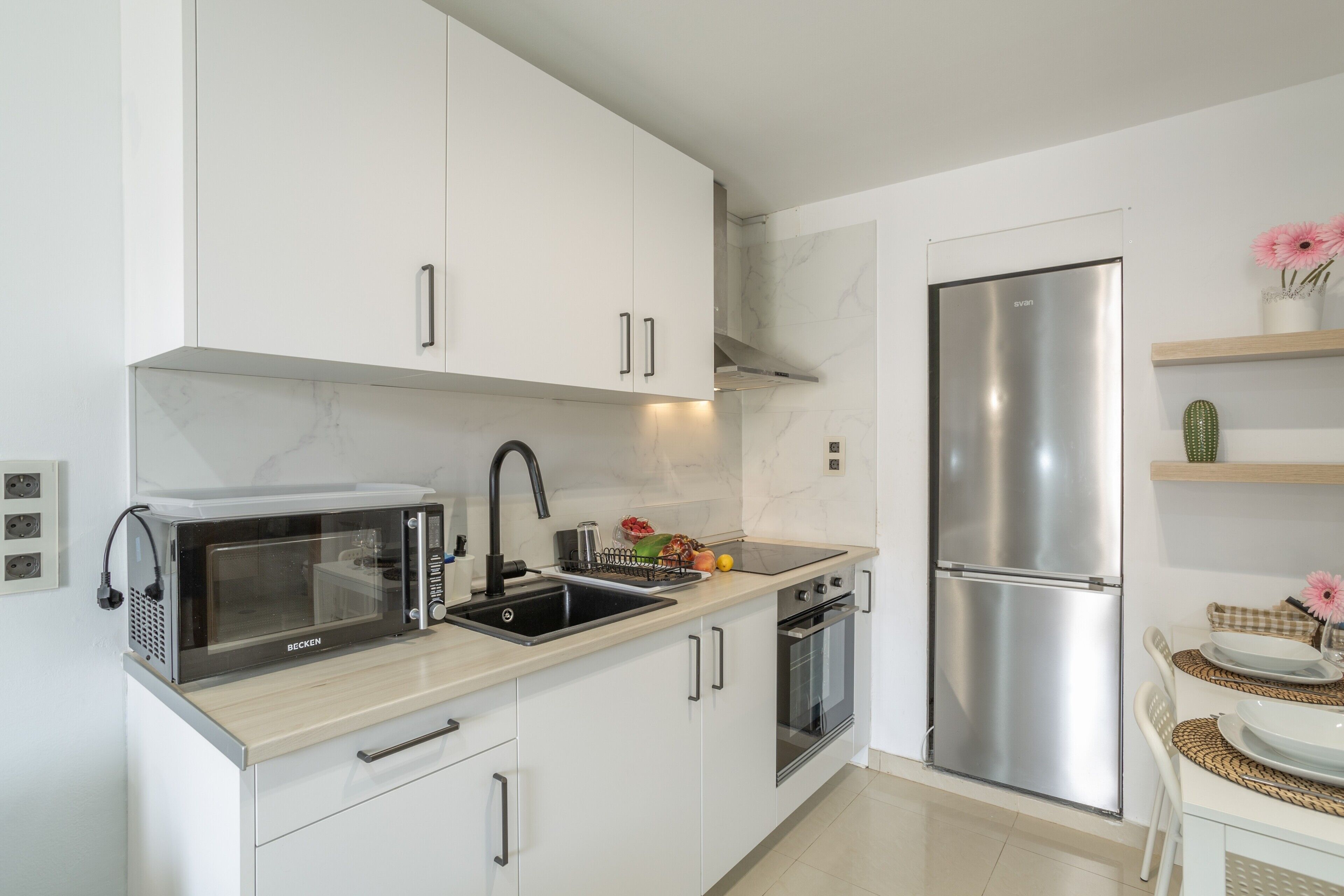 A modern kitchen with white cabinets, a microwave, a sink, a stove, and a refrigerator.