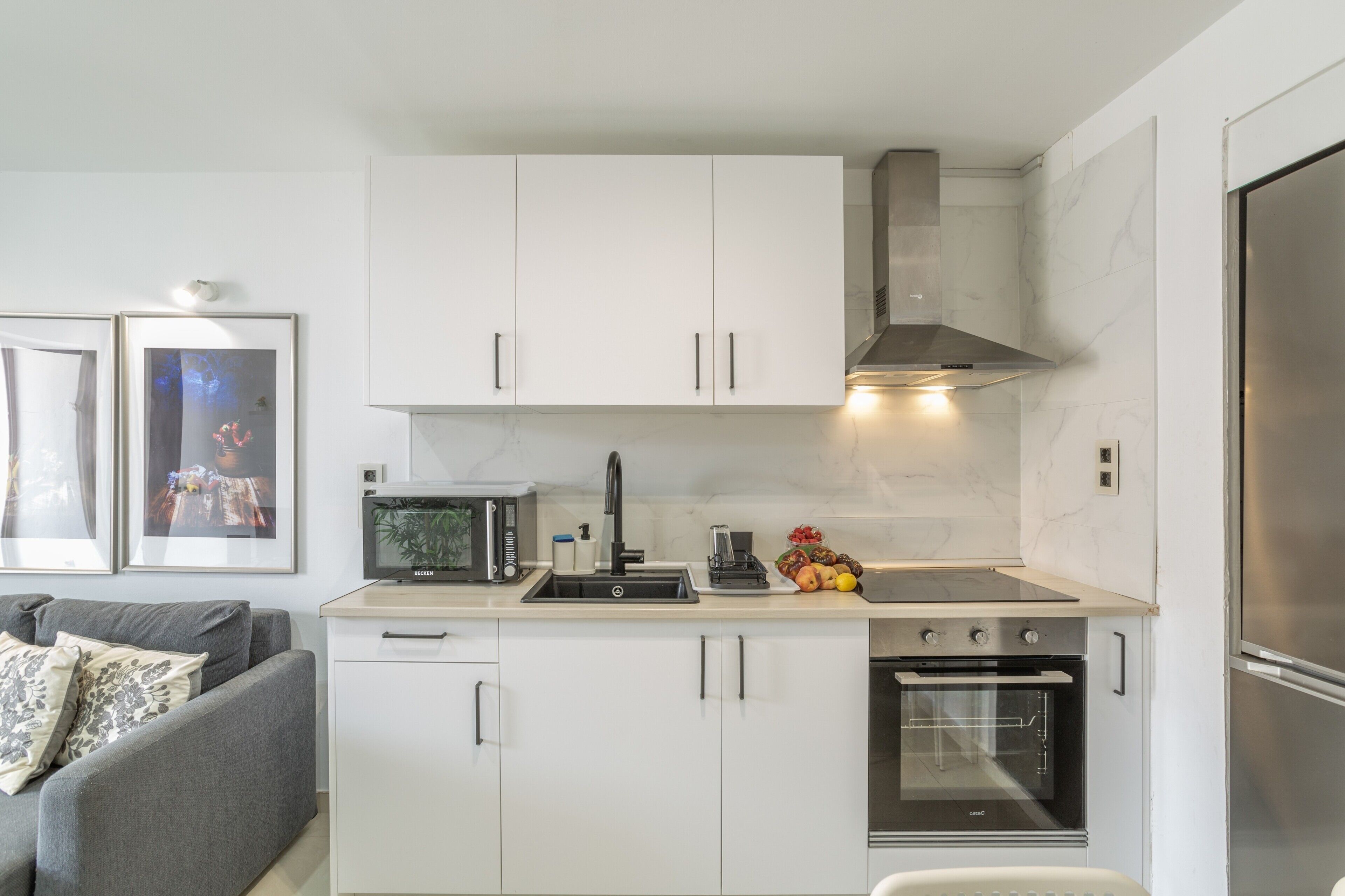 Een kleine keuken met witte kastjes, een inbouwoven, een magnetron en een rvs afzuigkap.