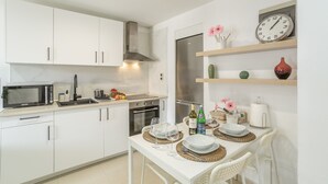 Een moderne keuken met witte kastjes, een magnetron, fornuis en oven. Er staat een eettafel gedekt met borden, glazen en een klok aan de muur.