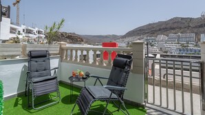 Een balkon met twee stoelen, een kleine tafel en uitzicht op een bergachtig landschap.