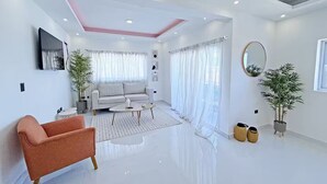 A modern living room with a sofa, coffee table, and a pink armchair. There are two potted plants and a round mirror on the wall. - Terrace Oasis w/ Private Jacuzzi and Stunning View (Puerto Plata)
