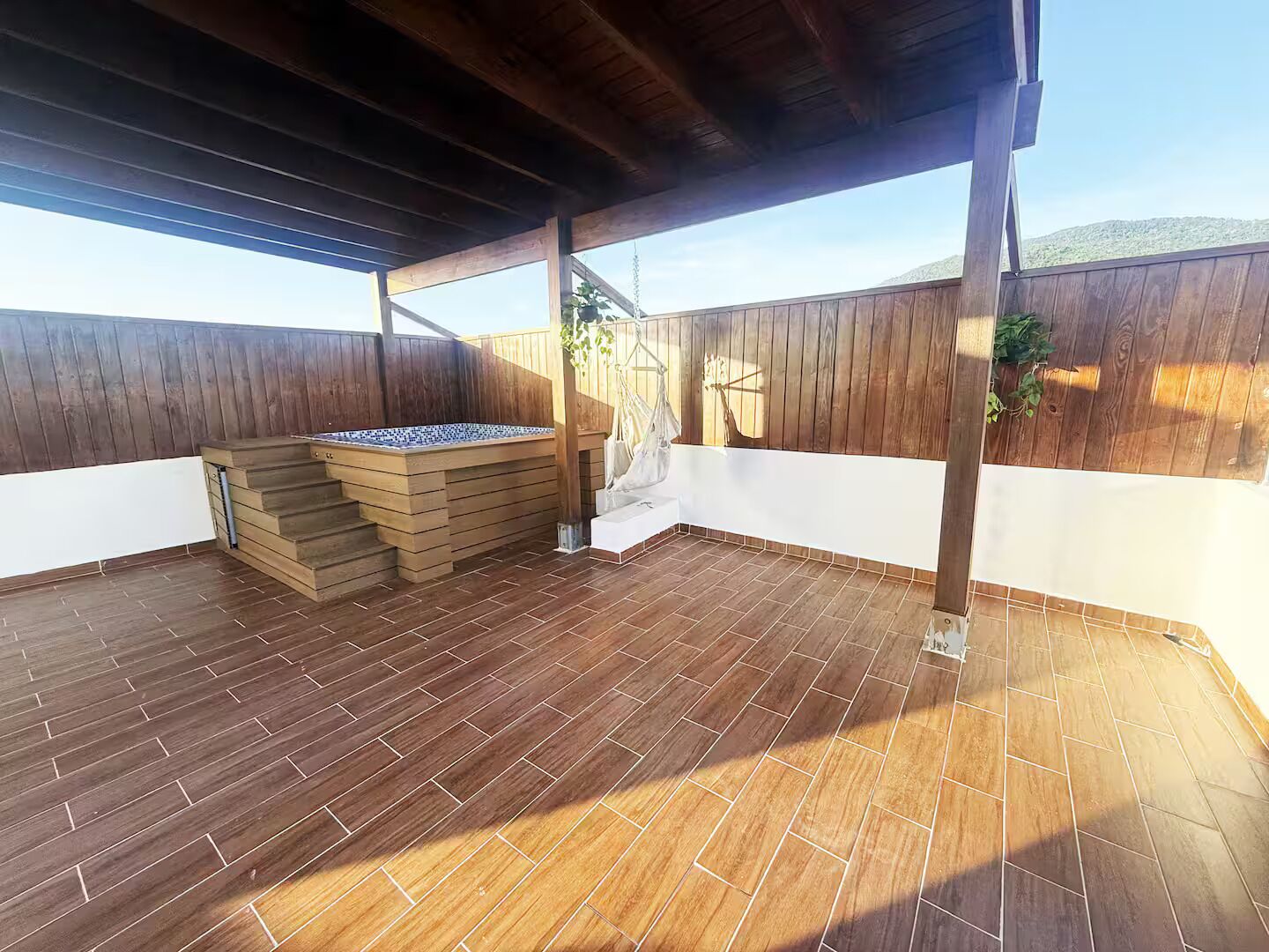 Un patio cubierto con un jacuzzi, escalones de madera y vistas del entorno.