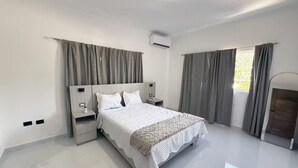 A modern bedroom with a large bed, bedside tables, an air conditioning unit, and a view of the outdoors through a window with curtains. - Terrace Oasis w/ Private Jacuzzi and Stunning View (Puerto Plata)
