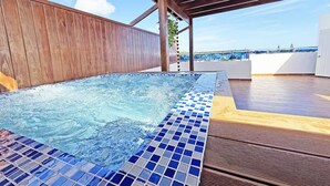 A hot tub with a tiled edge, wooden deck, and a view of the sea. - Terrace Oasis w/ Private Jacuzzi and Stunning View (Puerto Plata)