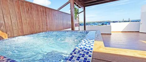 A hot tub with a tiled edge, wooden deck, and a view of the sea.