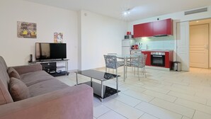 A modern living room with a sofa, TV, and glass coffee table. Adjacent is a kitchen with red cabinets, a microwave, and a stove. - Le Suquet - 2 bedroom - terrace (Cannes)