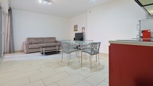 A modern living room with a sofa, a glass-top dining table, and chairs. There is a red cabinet and a television on the wall. - Le Suquet - 2 bedroom - terrace (Cannes)