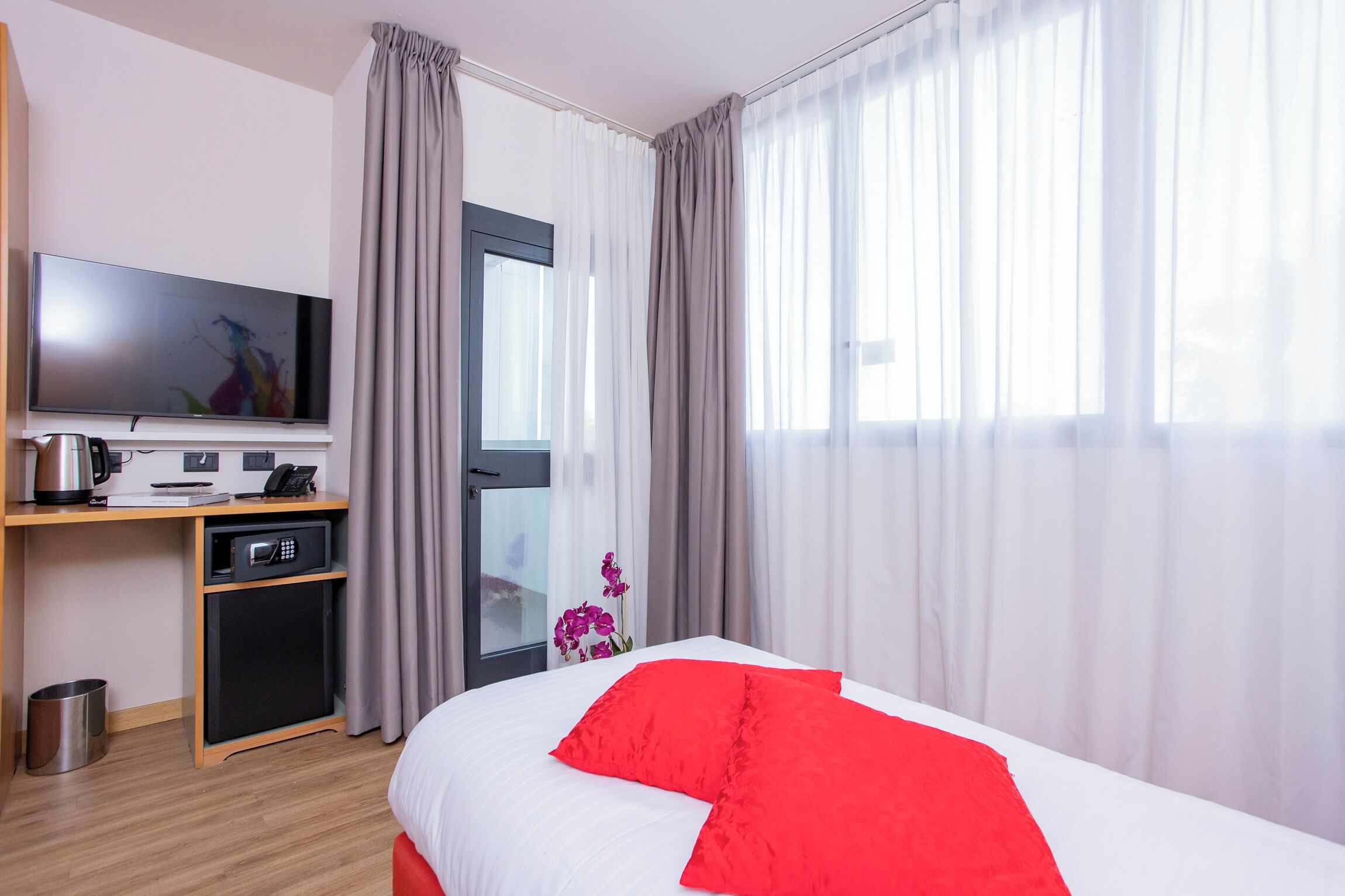 A hotel room with a bed, a TV, a desk with a microwave, and a small trash bin.