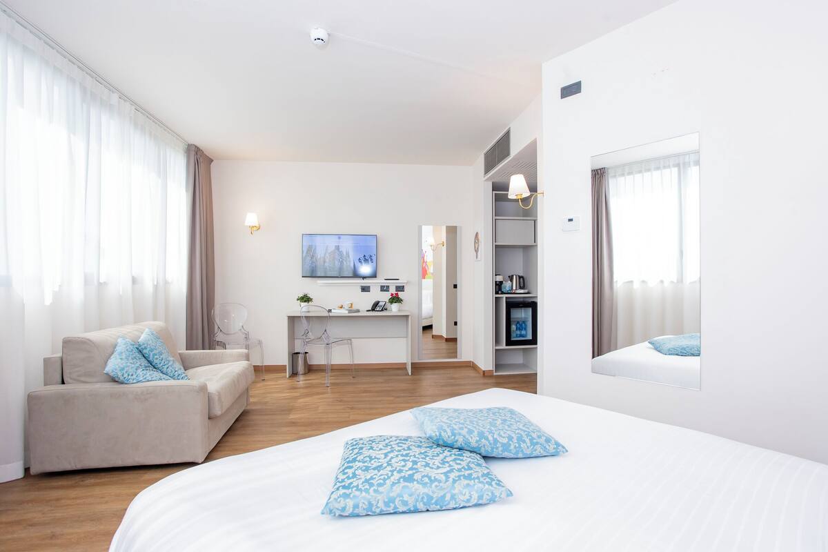 Ein modernes Hotelzimmer mit Bett, Sofa, Schreibtisch und Fernseher.