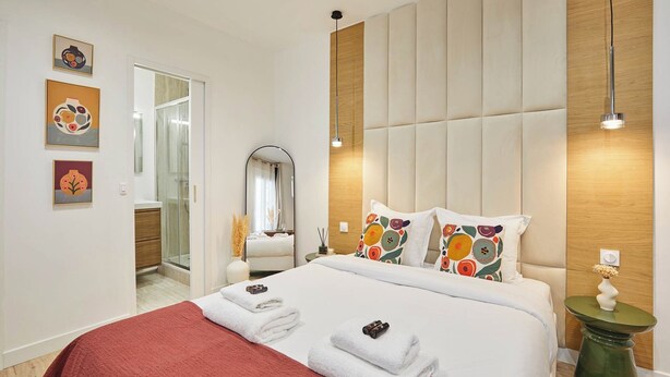 A modern hotel room with a large bed, a mirror, a bedside table with a lamp, and artwork on the walls. - Luxury Suite in the Center of Paris (Paris)