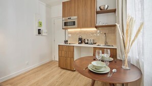 A modern kitchen with wooden cabinets, a built-in oven, and a dining area with a round table set for two. - Luxury Suite in the Center of Paris (Paris)