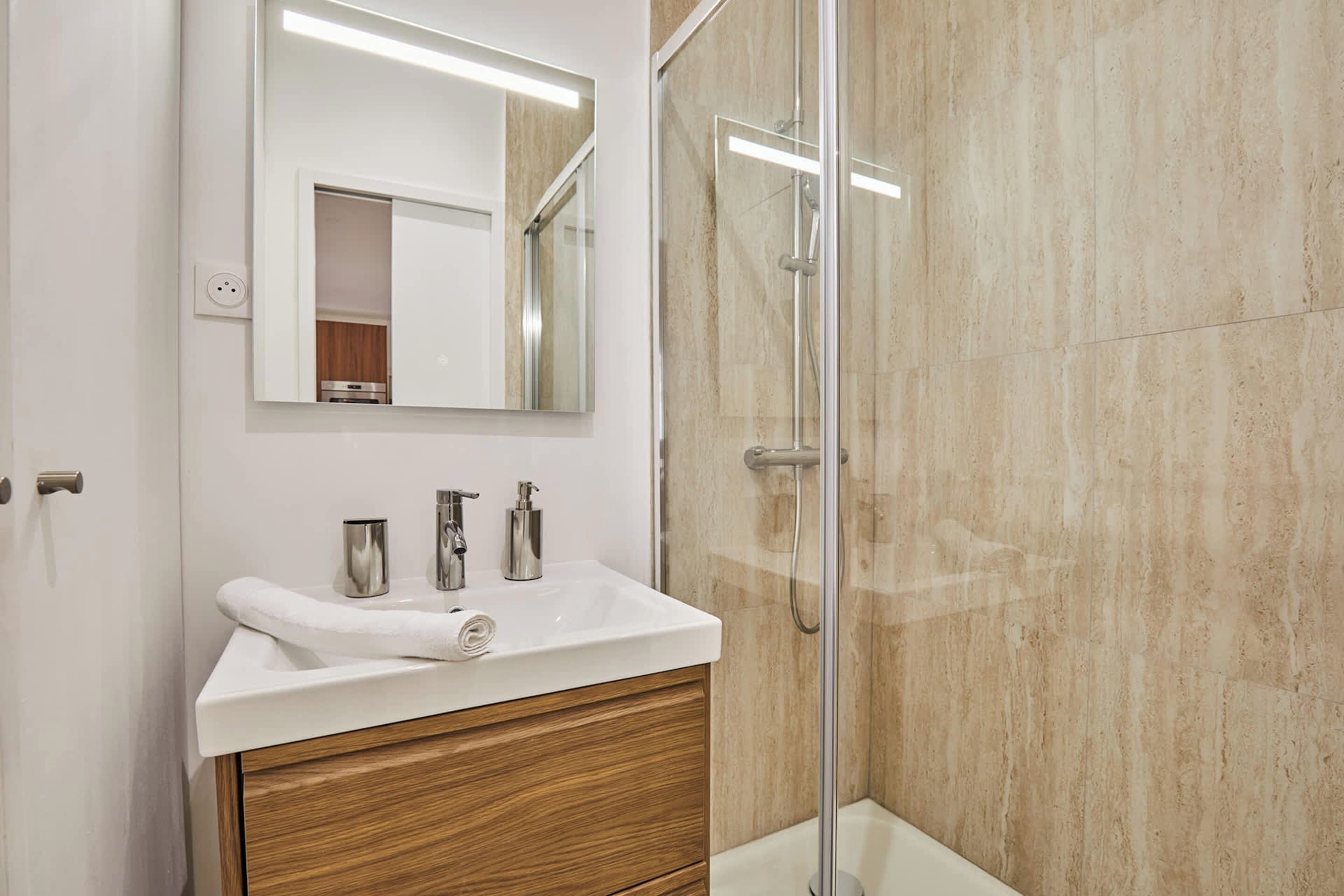 Une salle de bain moderne avec un lavabo blanc, un meuble-lavabo en bois et une cabine de douche en verre.