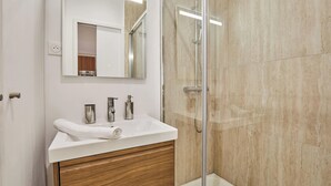 A modern bathroom with a white sink, wooden vanity, and a glass shower enclosure. - Luxury Suite in the Center of Paris (Paris)