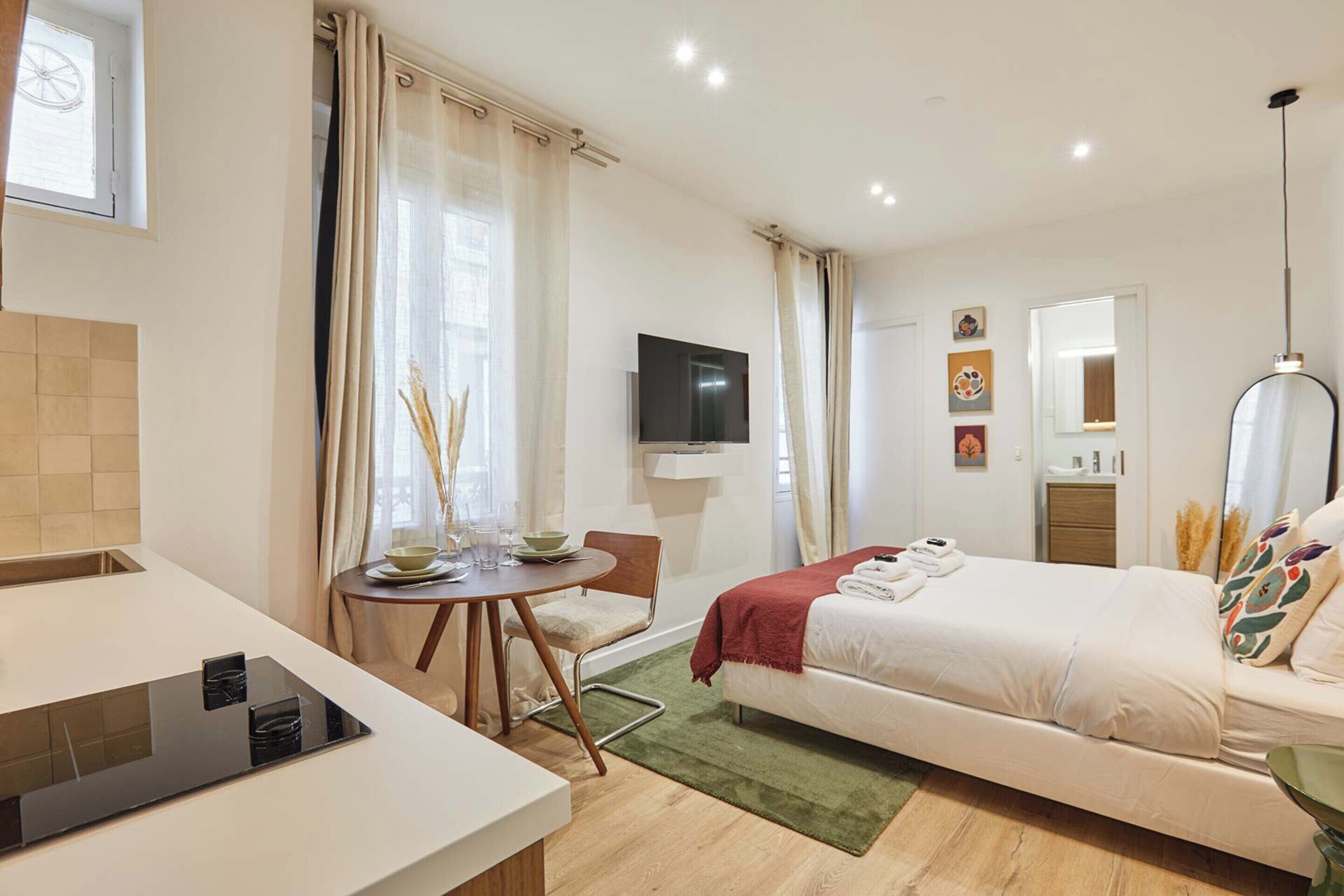 Une chambre d’hôtel moderne équipée d’un lit, d’un bureau avec un ordinateur portable, d’une télévision et d’un coin repas avec une table et des chaises.