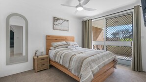 Een slaapkamer met een bed, nachtkastje en een raam met uitzicht.