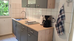 Cozinha moderna com armários cinza, bancada de madeira, pia, cafeteira e lixeira.