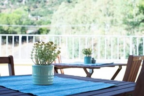 A wooden table with a blue placemat, a potted plant, and a view of a green landscape through a white railing. - Comfortable room with private balcony and view (Guspini)