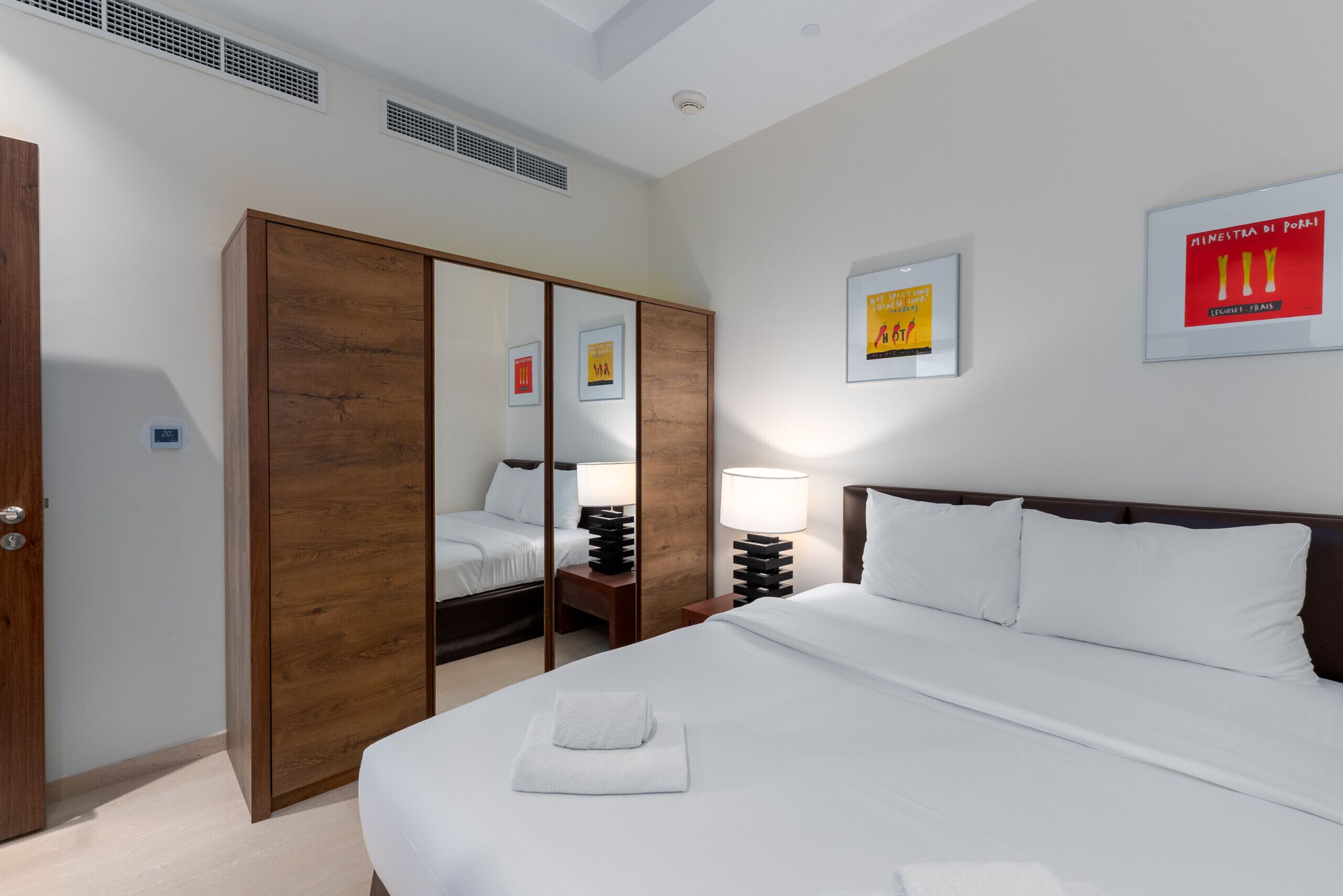 A hotel room with a large bed, a wooden wardrobe, a mirror, and framed pictures on the wall.