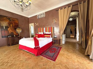 A spacious bedroom with a large bed, a decorative mirror, a chandelier, and a red and white striped headboard. - Palais Khemia (Marrakech)
