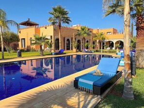 A swimming pool with lounge chairs, palm trees, and a building with arches. - Palais Khemia (Marrakech)