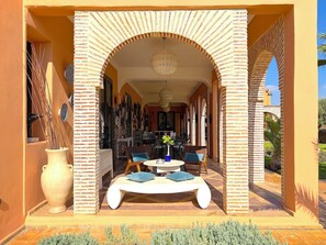 A covered outdoor seating area with a white bench and chairs, surrounded by brick arches and a hanging light fixture. - Palais Khemia (Marrakech)