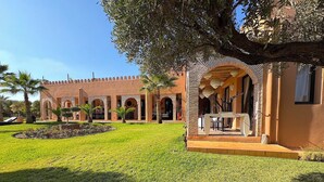 A courtyard with a pool, palm trees, and a building with arches and a tiled roof.