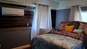 Une chambre à coucher avec un lit, un climatiseur fixé au mur et une fenêtre avec des rideaux.