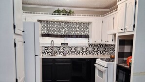 Une cuisine de taille réduite avec des meubles blancs, un crédence à motifs noir et blanc, une cuisinière à gaz et un four à micro-ondes.