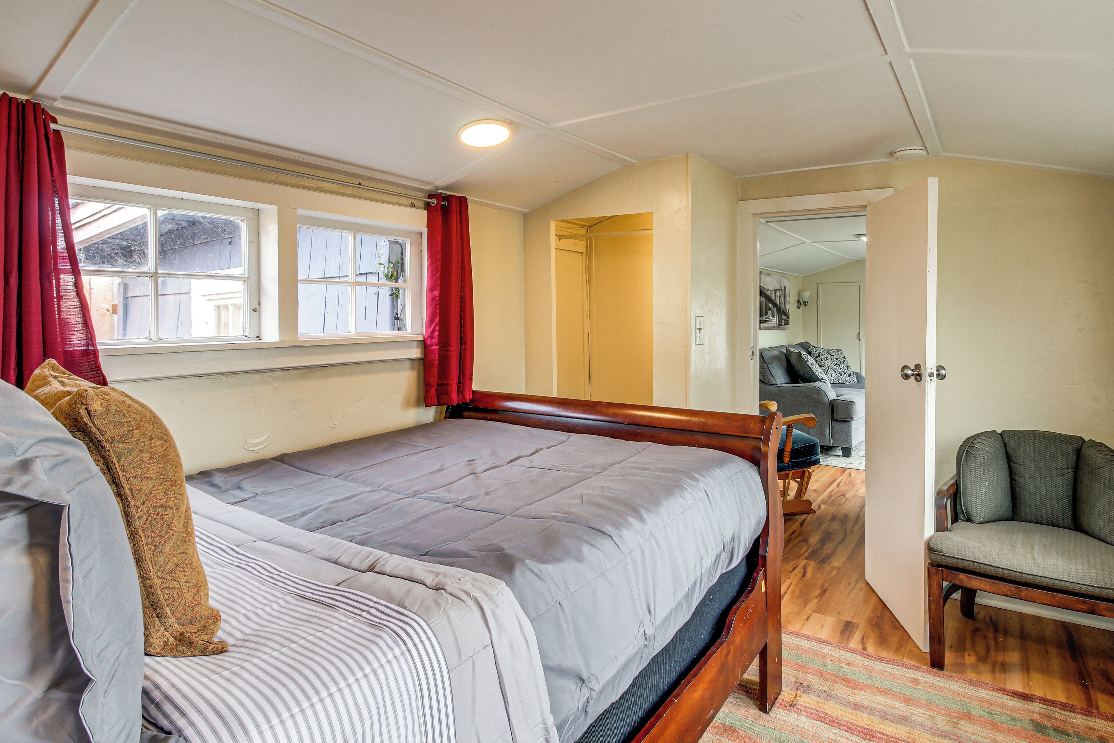 Un dormitorio con cama, una silla, una ventana con cortinas y una puerta que da a otra habitación.