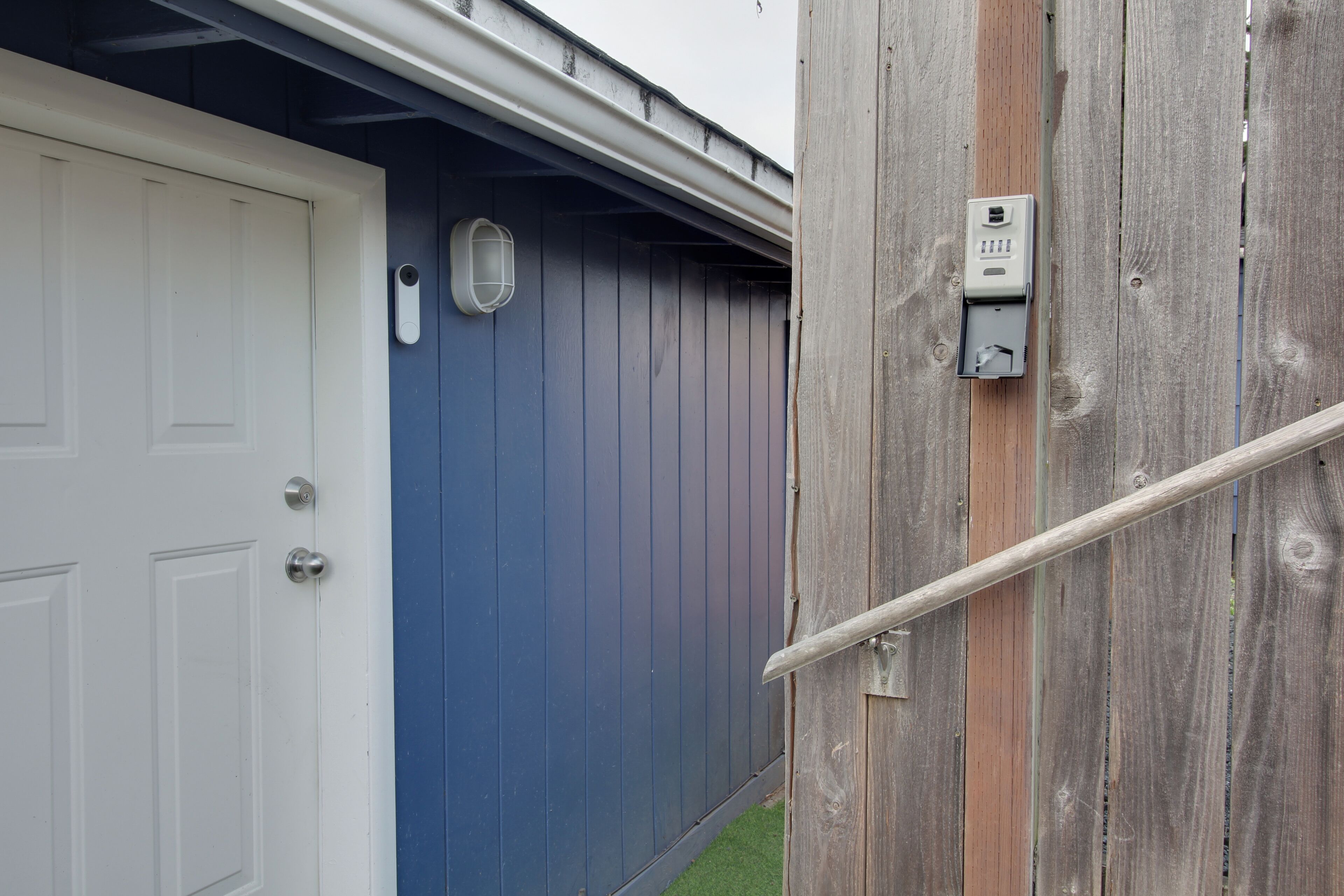 Une porte blanche avec une poignée argentée, une porte bleue et une clôture en bois avec un portail en métal.