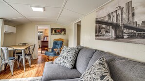 A living room with a gray sofa, patterned pillows, a wooden dining table with chairs, and a cityscape painting on the wall. - Quaint Coos Bay Escape, 2 Mi to Downtown (Coos Bay)