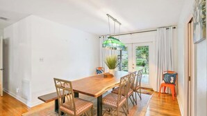 Un comedor con mesa y sillas de madera, una lámpara colgante y vistas al exterior con vegetación.
