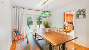 Un comedor con una mesa de madera, sillas, una lámpara colgante y vistas a la cocina por una puerta abierta.