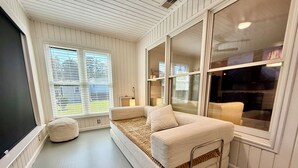 Ein Zimmer mit großem Fenster, einer Couch, einem kleinen Hocker und einem Fernseher.